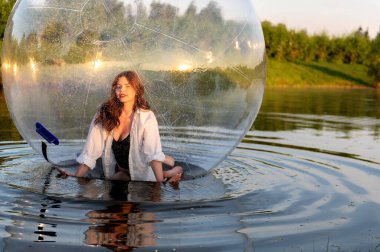 Water ball (similar to zorb or Human Hamster Ball) with young woman inside on pond surface clipart