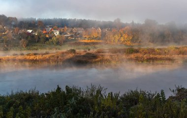 Autumn fog over the river water and colorful roofs of small town houses in the distance clipart