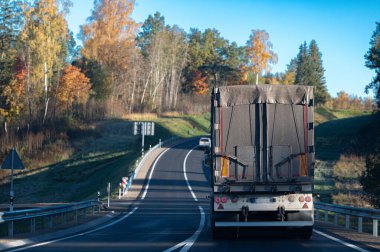 Sonbaharda asfalt bir yolda bir kamyon ve yaklaşan arabalarla bir viraj.