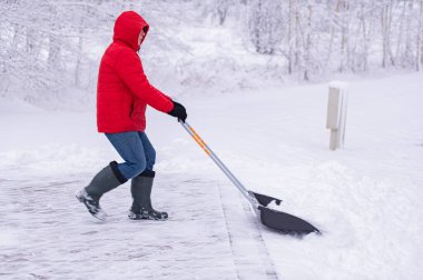 Bir adam kar küreğiyle kaldırımı temizliyor..