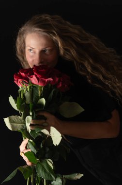 Makyajsız, olgun, doğal bir kadın. Siyah üzerinde kırmızı güller olan güzel bir kadın. Güzel stüdyo portresi. Kırmızı gülleri olan güzel bir model.