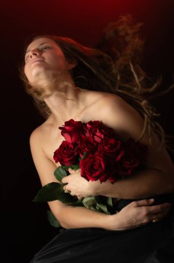 Stüdyonun arka planında çıplak omuzları ve kırmızı gülleri olan seksi bir kadın. Güzel stüdyo portresi. Siyah üzerine izole edilmiş kırmızı güllü şehvetli bir model. Makyajsız, olgun, doğal bir kadın..