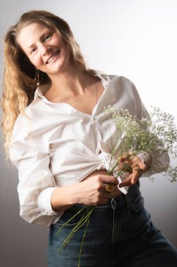 Beyaz gömlekli, kot pantolonlu, elinde çiçekle güzel bir kadın.