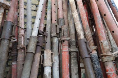 A close-up view of various metal scaffolding pipes stacked together. The pipes are of different colors, including red, gray, and brown, showcasing signs of wear and rust. The background features a textured wall. clipart