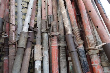 Çeşitli inşaat malzemelerinin ve yapı iskelesi tüplerinin yakın çekim görüntüsü. Tüpler farklı renk ve dokulara sahip metalden yapılmış, bazı aşınma ve pas izleri var. Düzenleme görsel olarak ilginç bir patte oluşturur