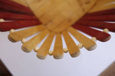 Alternatif kırmızı ve sarı çıtçıtlı, aralarında küçük yuvarlak tahta boncuklar bulunan dekoratif ahşap bir nesnenin yakın çekim görüntüsü. Tasarım benzersiz bir desen ve işçilik sergiliyor..
