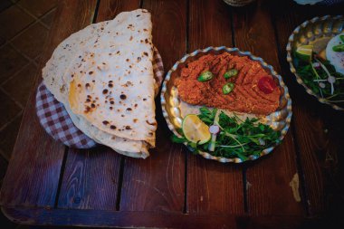 Düz ekmek ve yeşil biber, limon dilimleri ve taze otlarla süslenmiş bir tabak baharatlı kırmızı sos içeren geleneksel bir yemek kırsal ahşap bir masada servis edilir..