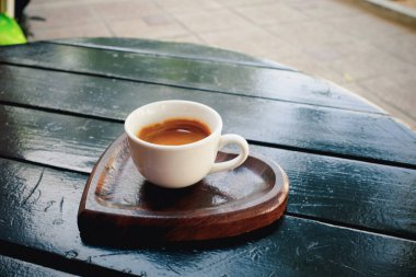 Kalp şeklinde ahşap bir tepsi içinde espresso dolu küçük beyaz bir kahve fincanı. Bardak, pürüzsüz bir kaplama ile koyu ahşap bir masaya yerleştirilir ve arka planda bulanık dış unsurlar vardır..