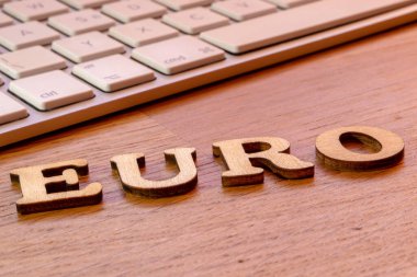 Arkaplanda beyaz klavye ve Avrupa para birimi başlığı bulunan ahşap masa üzerinde euro yazıları
