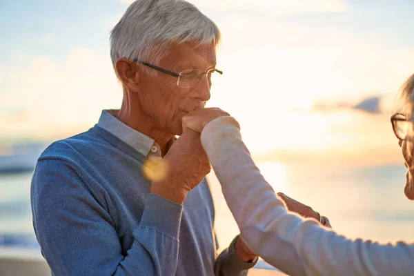恋に高齢者のインテリジェントなカップルロマンチックな海では ビーチでの時間を過ごす 優しくお互いに抱擁 妻の手にキスをする老人 — ストック写真