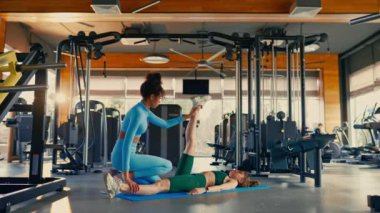 Spor giyim sektöründe Afrikalı ve Kafkas kökenli zayıf kadınlar spor salonunda lastik paspasın üzerinde uzanırken esneme egzersizleri yapıyorlar. Spor ve eğlence kavramı..