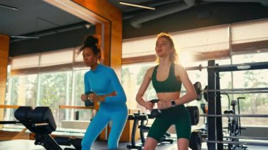 Spor giyimli zayıf atletik beyaz ve Afrikalı Amerikalı kadınlar spor salonunda kettlebell ile çömeliyor. Spor ve eğlence kavramı..