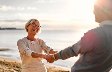 Yaşlı ve zeki çift deniz kenarında romantik bir şekilde vakit geçiriyorlar, el ele tutuşuyorlar ve nazikçe sarılıyorlar..