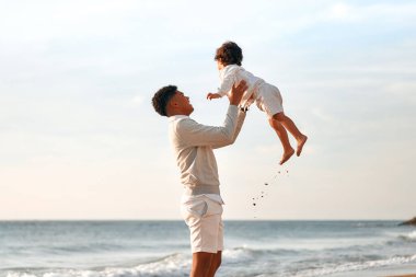 Afrika kökenli Amerikalı bir aile deniz kenarındaki kumlu sahilde eğleniyor. Küçük oğluyla birlikte sahilde yürüyüp eğlenen genç bir baba..