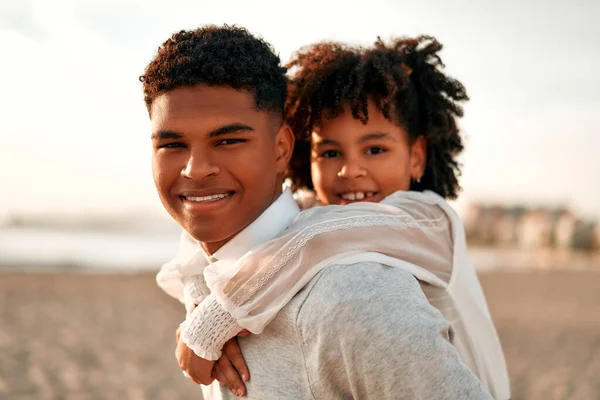 海沿いの砂浜で楽しいアフリカ系アメリカ人の家族 弟とともに彼の可愛いです妹オン彼の背中の再生オンザビーチ — ストック写真