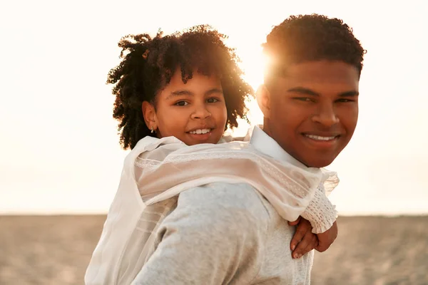 海沿いの砂浜で楽しいアフリカ系アメリカ人の家族 弟とともに彼の可愛いです妹オン彼の背中の再生オンザビーチ — ストック写真