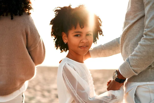 アフリカ系アメリカ人の家族で可愛いです巻き娘で白いドレスを手に海の近くの砂浜を歩いて夜明け — ストック写真