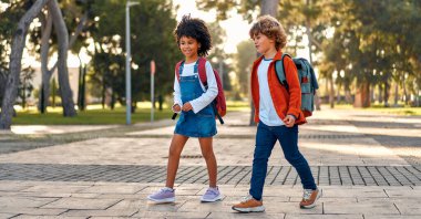 Okul çantalı mutlu akıllı çocuklar okula koşuyor. Okula dönelim. Okuldan sonra bir Afrikalı Amerikalı kız ve sınıf arkadaşı sokakta yürüyorlar..