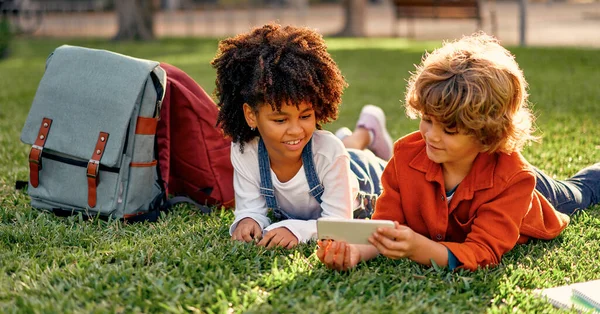 可爱的学童躺在公园的草地上 一边打电话一边玩游戏 回学校去非洲裔美国女孩和白人可爱男孩放学后玩得开心 — 图库照片