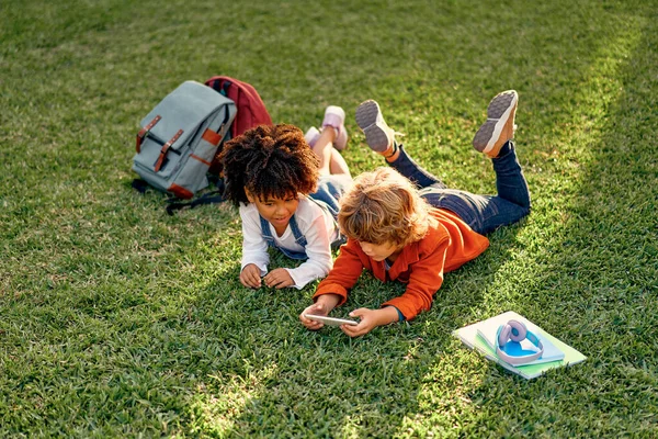 Bedårande Skolbarn Spelar Spel Telefonen Medan Ligger Gräset Parken Tillbaka — Stockfoto