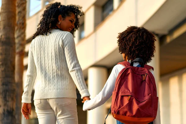 Happy African American mother and daughter preschool student walking to school. Beginning of lessons. First day of fall. Parenthood or love and bonding expression concept.