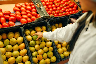 Genç bir kadın limonları dükkandan seçer. Taze sebze ve meyve alıyorum. Sağlıklı yiyecekler. Limon ve domates sandıkları satılıktır..