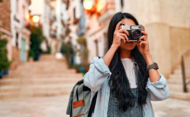 Portrait of asian female tourist or student walking and making photos on retro camera on city streets. Vacation and tourism concept.