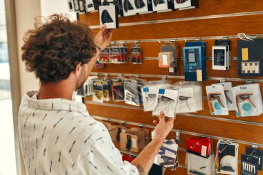 Handsome bearded curly man choosing a guitar capo in a musical instrument store. Hobbies and recreation. Purchase of accessories for musical instruments.