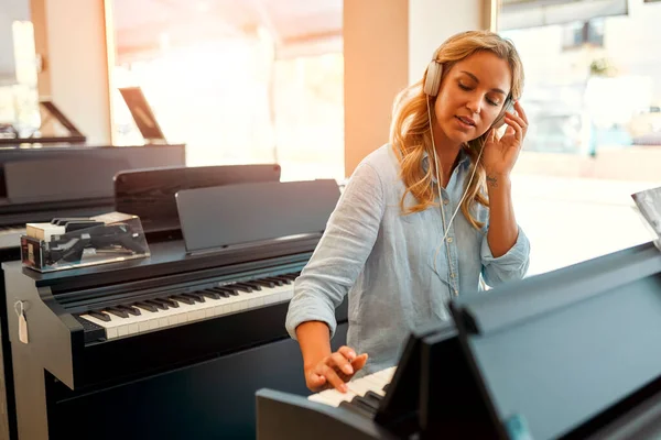 Young beautiful woman in headphones sitting at the piano and playing it in a musical instrument store. Hobbies and recreation. Buying a piano in a store.
