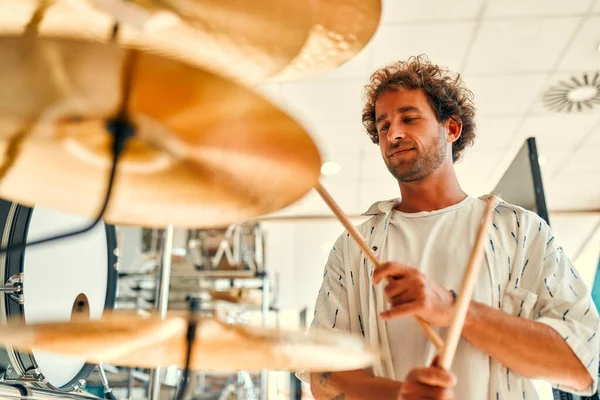 Handsome bearded curly man choosing a drum kit in a musical instrument store. Hobbies and recreation. A man buying a drum in a store and trying to play it.