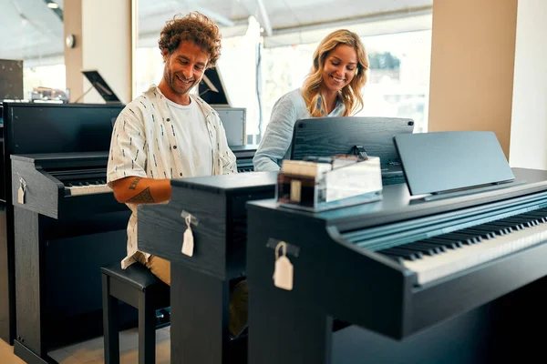 Young couple sitting at the piano and playing four hands in a musical instrument store. Hobbies and recreation. Buying a piano in a store.