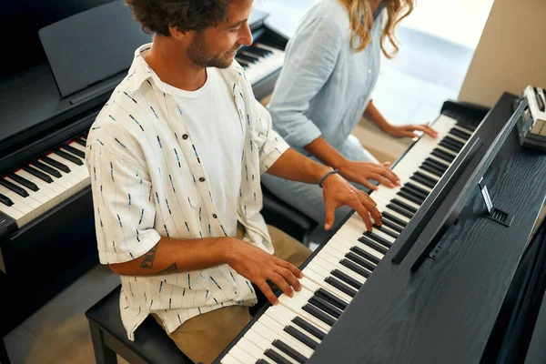 Young couple sitting at the piano and playing four hands in a musical instrument store. Hobbies and recreation. Buying a piano in a store.