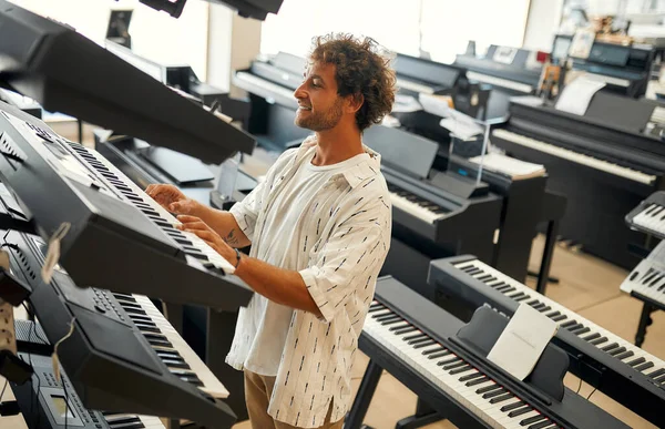 Young attractive man choosing a piano or synthesizer in a musical instrument store. Hobbies and recreation. Buying a midi keyboard in a store.