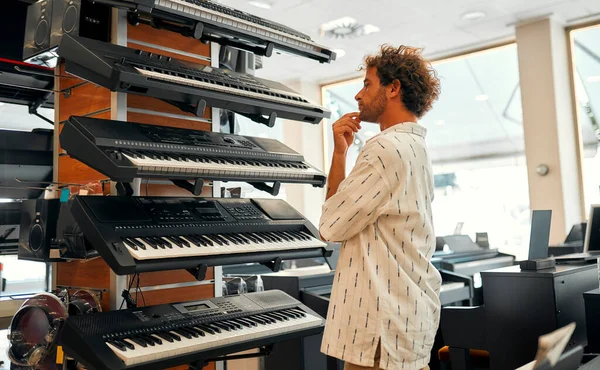 Young attractive man choosing a piano or synthesizer in a musical instrument store. Hobbies and recreation. Buying a midi keyboard in a store.