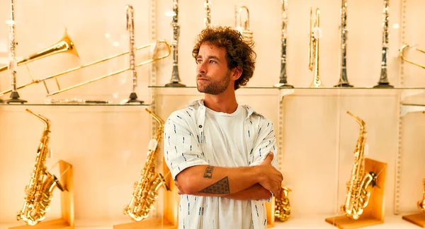 A young attractive man standing in front of a showcase with wind instruments in a musical instrument store. Hobbies and recreation.