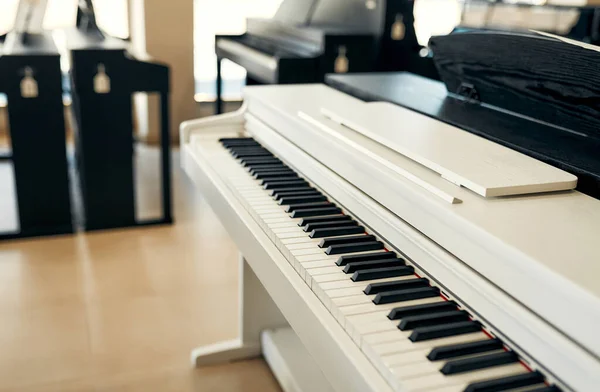 Close-up of a white piano in a musical instrument store. Lots of different keyboard instruments for sale. Hobbies and recreation.