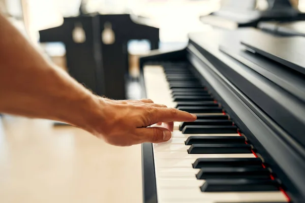 Close-up of a man\'s hand playing the keys of a black piano in a musical instrument store. Lots of different keyboard instruments for sale. Hobbies and recreation.