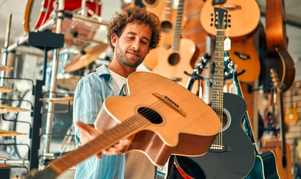 Handsome bearded curly man choosing a guitar in a musical instrument store. Hobbies and recreation.