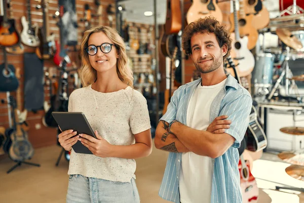 Sales consultants standing in a musical instrument store against the backdrop of walls with many different guitars. Buying a guitar and musical instruments.