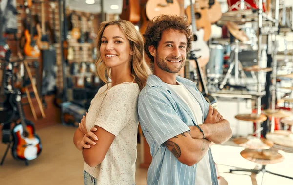 Sales consultants standing in a musical instrument store against the backdrop of walls with many different guitars. Buying a guitar and musical instruments.