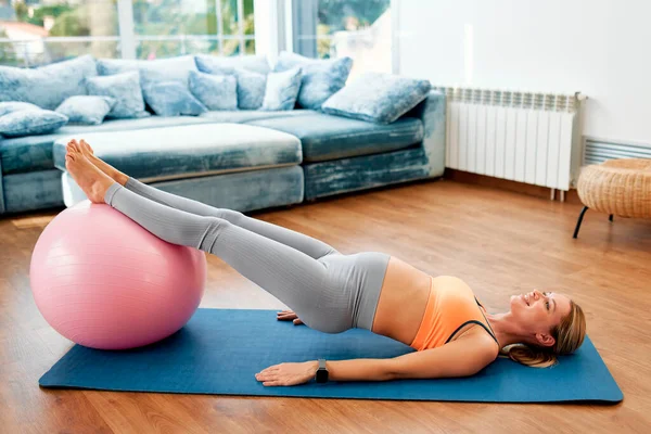 一位穿着运动服的年轻孕妇在客厅的橡胶垫子上做运动 带着一个健身球 怀孕期间的运动 — 图库照片