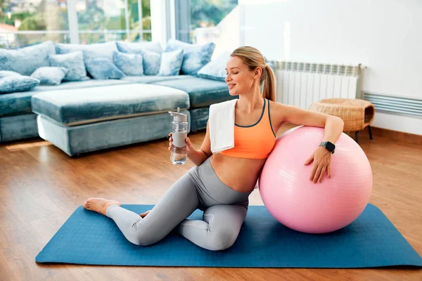 一名穿着运动服的年轻孕妇在家里客厅里锻炼之后 身穿运动服 坐在橡皮垫上 拿着一个健身球 怀孕期间的运动 — 图库照片