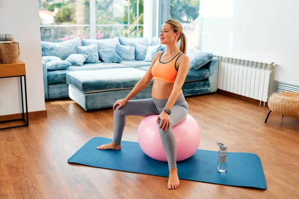一位穿着运动服的年轻孕妇坐在健身球上和客厅里的橡胶垫子上做运动时 穿着运动服 怀孕期间的运动 — 图库照片