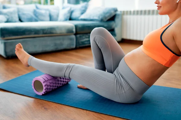一名穿着运动服的年轻孕妇在运动后 坐在客厅的橡胶垫子上 用按摩器按摩她的腿 怀孕期间的运动和瑜伽 — 图库照片