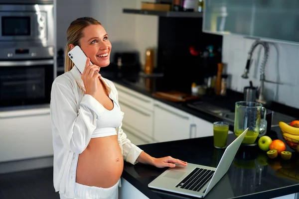 Genç Hamile Bir Kadın Mutfakta Dizüstü Bilgisayarının Başında Çalışıyor Telefonla — Stok fotoğraf