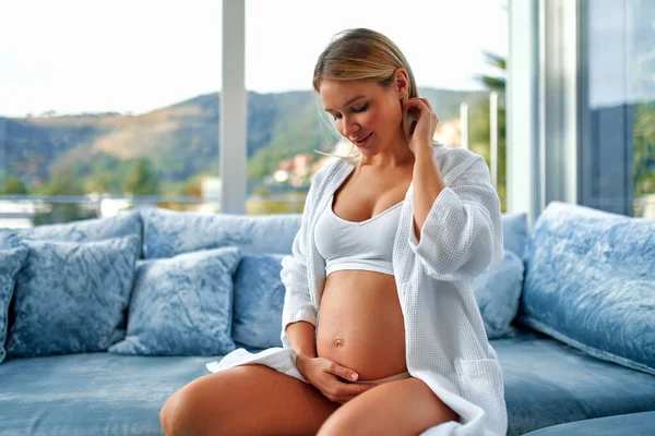 Молодая Беременная Женщина Белом Халате Руками Животе Сидящая Бархатистом Синем — стоковое фото