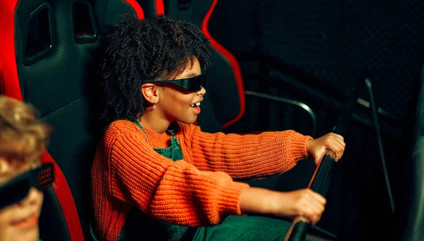 一个非裔美国女孩和一个可爱的白人男孩戴着眼镜坐在虚拟电影院里 一边移动着椅子 一边在游乐园里看电影 — 图库照片