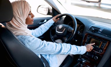 Bir arabanın direksiyonunda oturan tesettürlü genç Müslüman kadın. Bir araba alıp kiralamak. Seyahat ve eğlence..