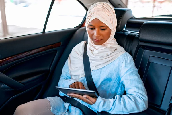 車の中で座っている間 タブレットを使用してヒジャーブの若いイスラム教徒の女性 車の中で働くイスラム教徒のビジネス女性 — ストック写真