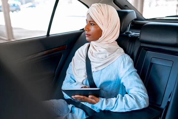 Young muslim woman in hijab using a tablet while sitting in a car. Muslim business woman working in the car.